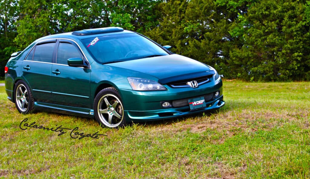 Team Hi Def A customized green Honda sedan, sporting JDM-inspired aftermarket wheels and a hood visor with the "HDF" logo, is parked on a grassy area with trees in the background. The photographer's signature graces the bottom left corner, highlighting this exotic car among any car club enthusiasts.